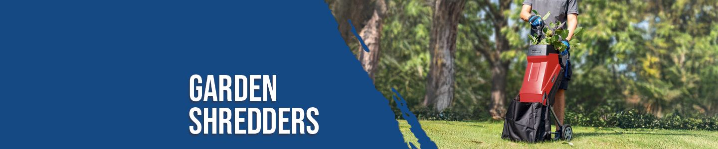 A Scheppach garden shredder in use. A person is pushing the shredder over a lawn, chopping up branches. Trees and bushes are visible in the background.