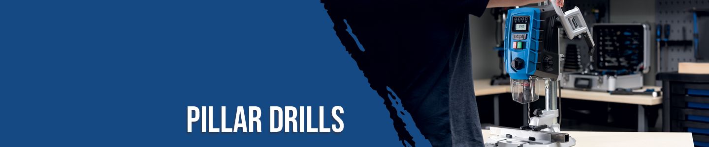 A worker operates a pillar drill in a workshop. The machine features a digital display and is mounted on a workbench. Additional tools and equipment are visible in the background.