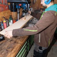 Person operating a Scheppach bench pillar drill DP16SL in a workshop setting