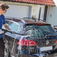 Man cleaning a car exterior with high-pressure cleaner near a Scheppach tool