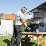 Man operating a Scheppach HL460 log splitter on a wooden table with wood logs nearby
