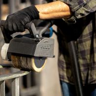 Scheppach metal wire brush in use on a machine. The brush is operating and being held by a person.