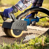 Scheppach metal wire brush in use on a machine. The brush is positioned on a wooden board and held by a person.