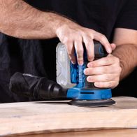 Scheppach cordless random orbital sander in use with handle, showing operational handling