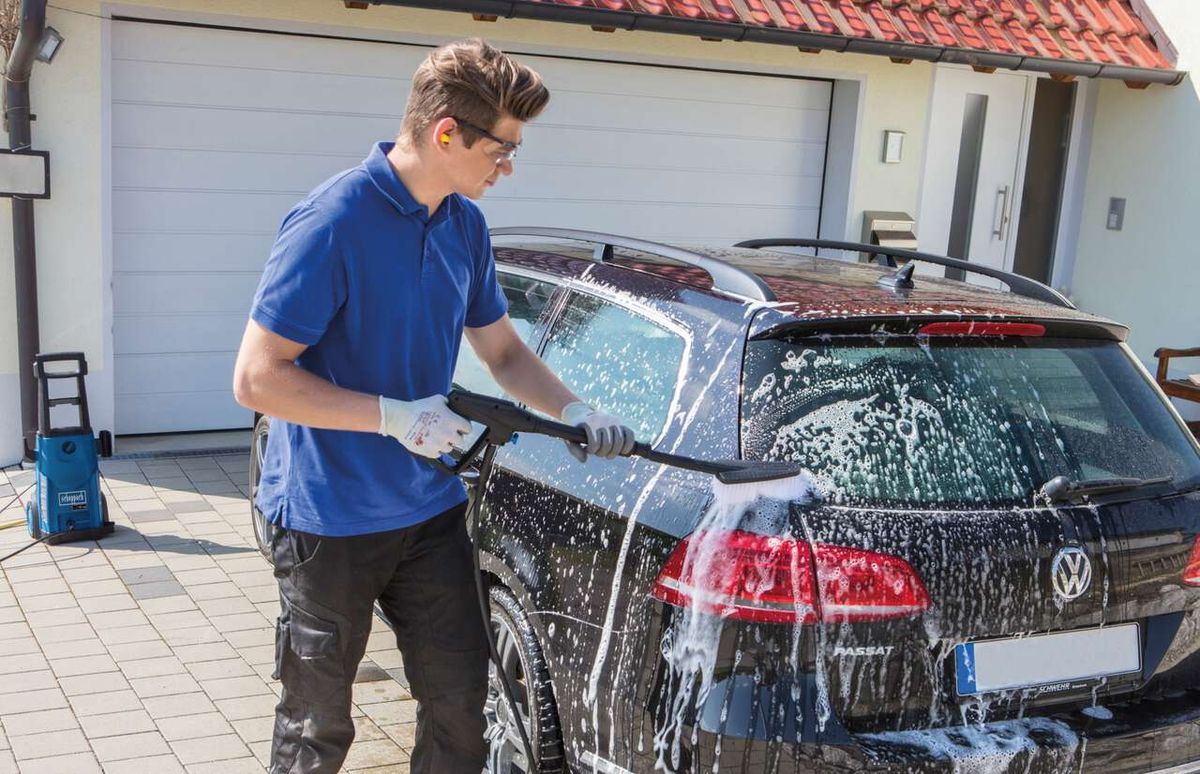 Man cleaning a car exterior with high-pressure cleaner near a Scheppach tool