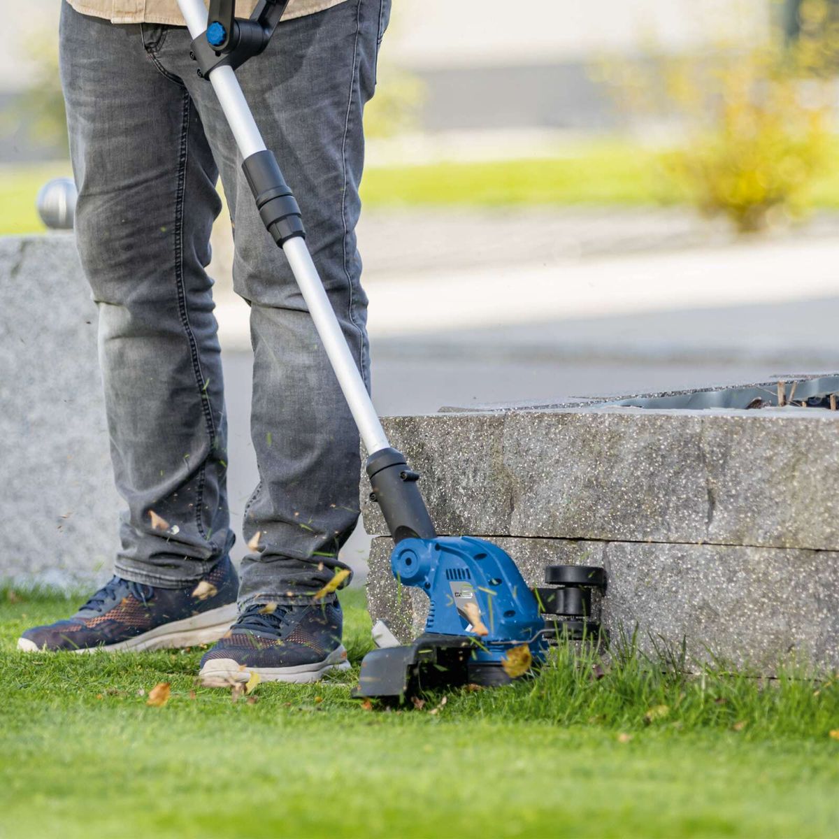 Person using cordless strimmer with cane support on grass