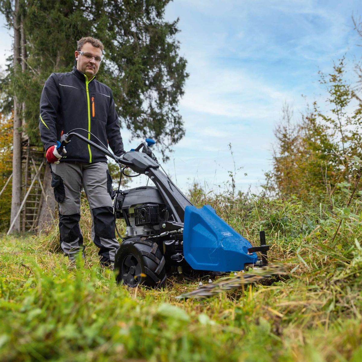 Person operating Scheppach lawnmower (BMS196-88) on a trail, cutting deck with collection bin