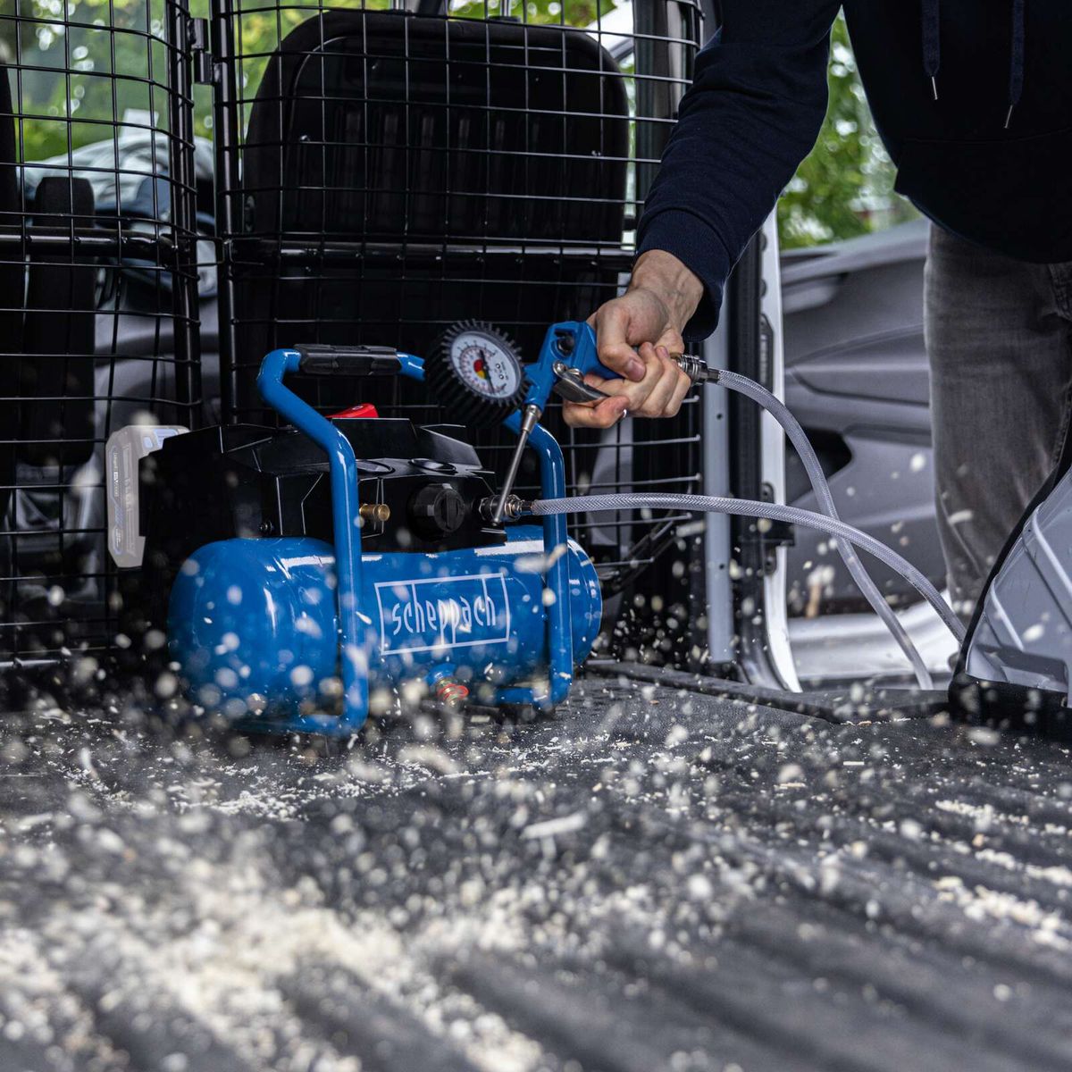 Scheppach cordless air compressor with pressure gauge and hose connection, showing spray mist