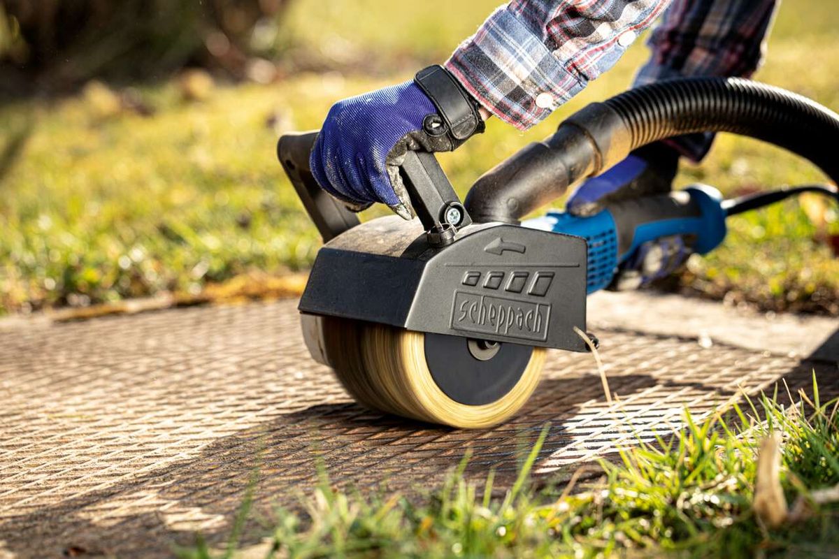 Scheppach metal wire brush in use on a machine. The brush is positioned on a wooden board and held by a person.