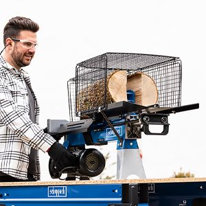 A man operates a Scheppach firewood splitter machine. The machine features a basket for logs and a hydraulic cylinder for splitting.